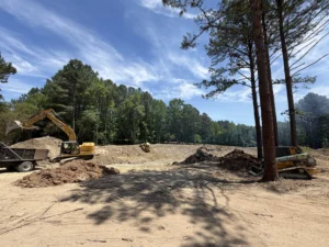 Heavy equipment excavating and grading a custom half-acre pond surrounded by trees during a pond construction project in Creedmoor, North Carolina.